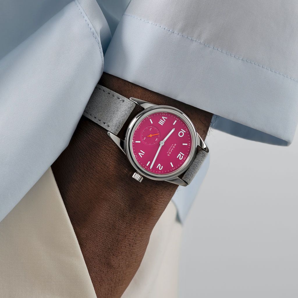 wrist with a pink faced watch. Wrist is in a pocket. Person is wearing a white shirt with cream pants