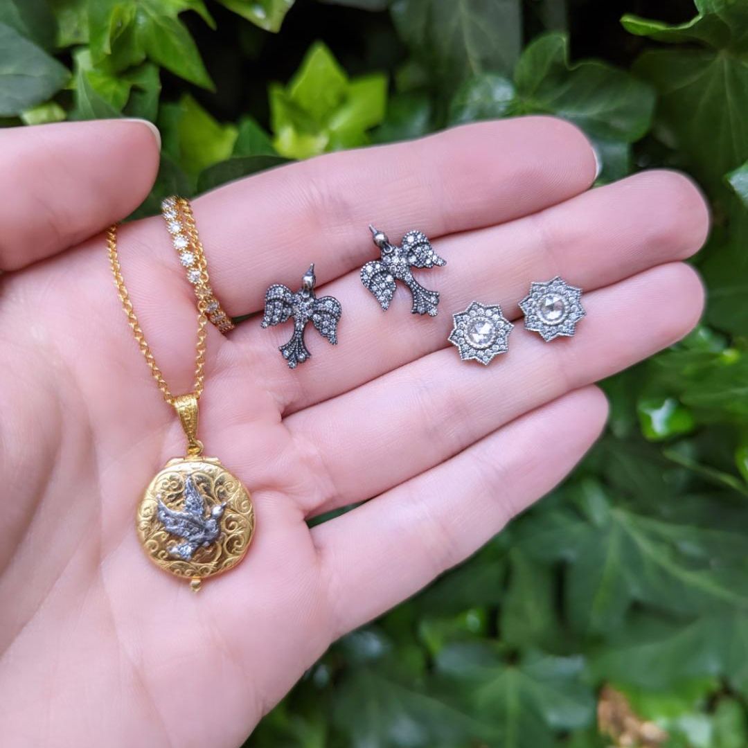 Hand holding two pairs of silver earrings and one gold pendant