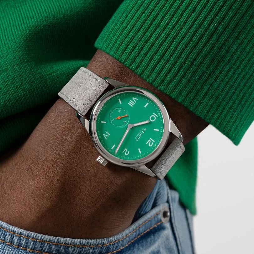 stainless steel watch with green dial on a wrist with hand in pocket. Model is wearing a green sweater
