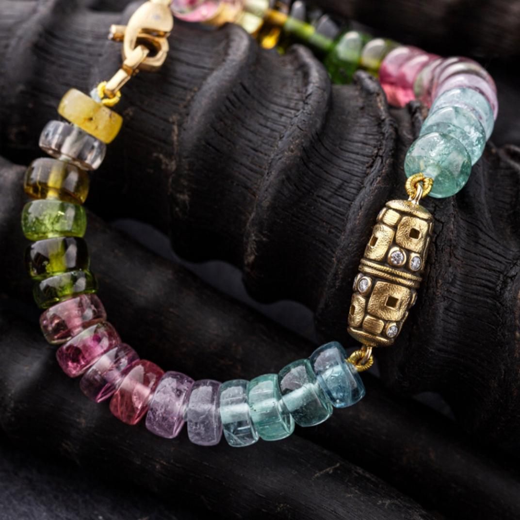 rainbow tourmaline and yellow gold bracelet on a dark background