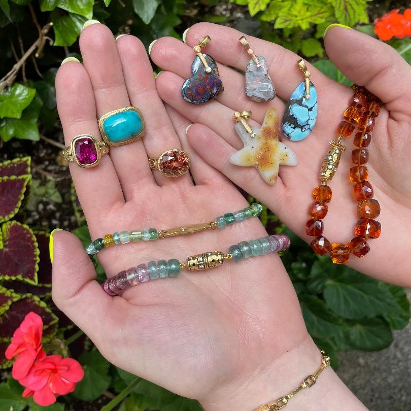yellow gold and gemstone jewelry spread out in two hands over green leaves