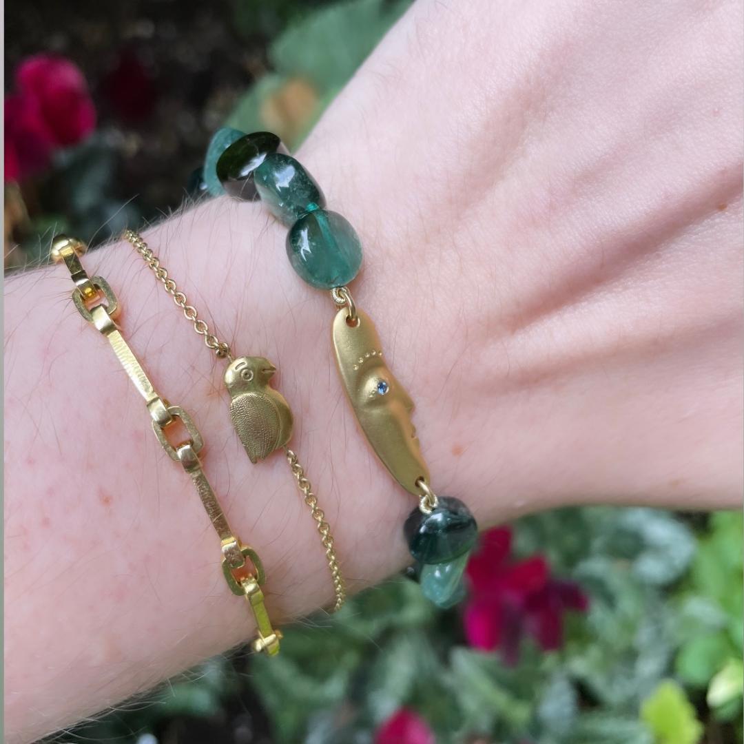 Close up photo of a wrist wearing 3 gold bracelets. One has tourmaline beads