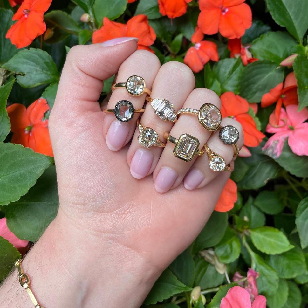 hand with 8 yellow gold and diamond engagement rings in front of flowers