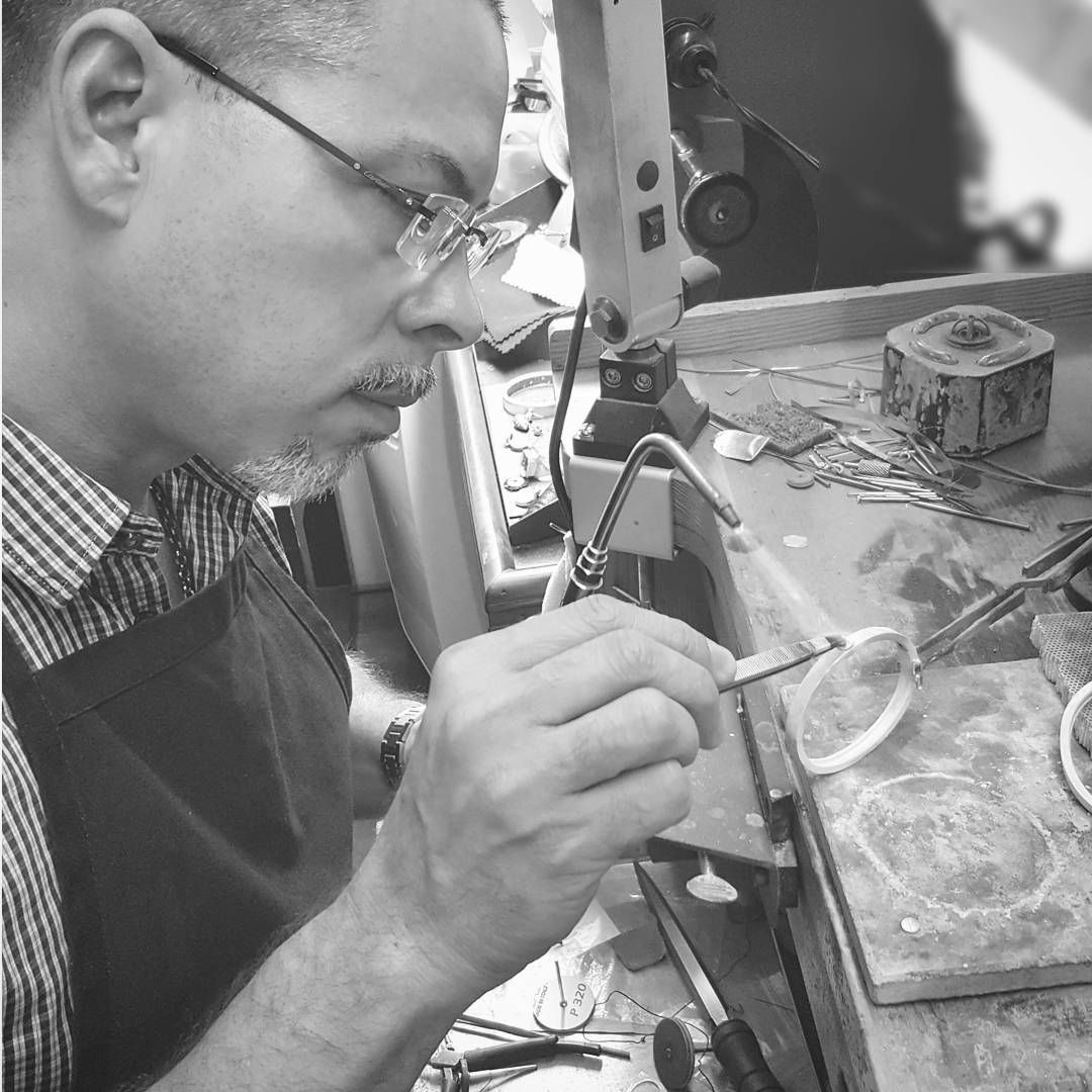 photo of a man with glasses working on jewelry at a bench