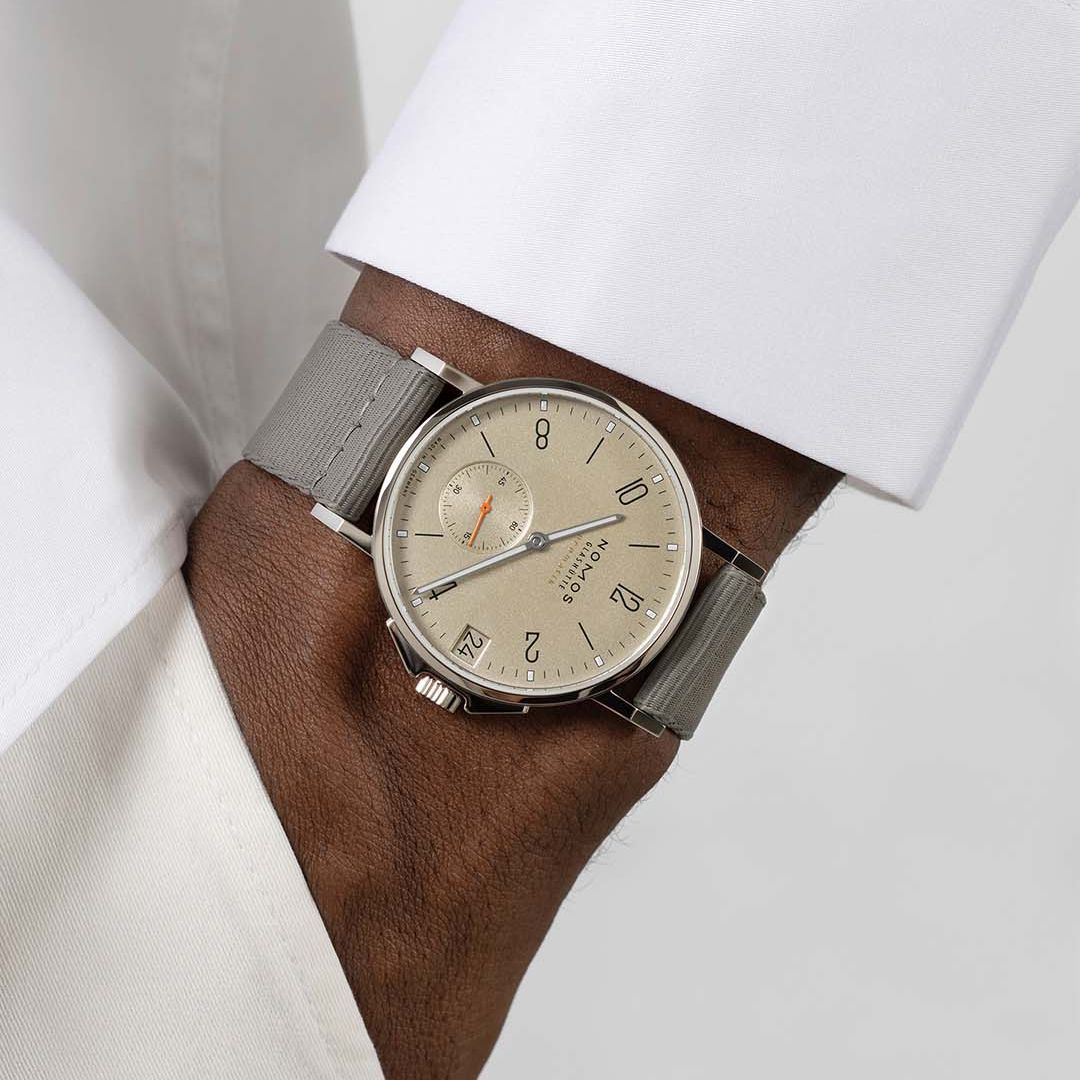 photo of hand in pocket with a watch on. Watch has a sand colored dial. Person is wearing all white.