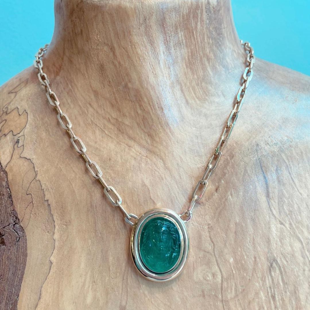 wood bust with gold necklace featuring a large emerald gemstone
