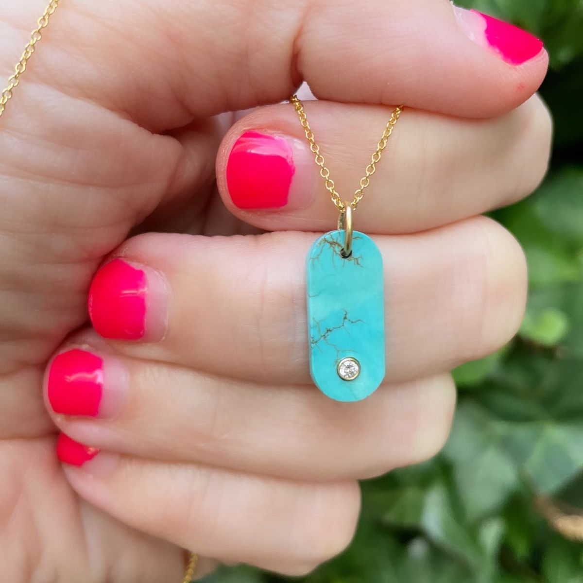 tourquoise gem tab being held in a hand with bright orange nail polish
