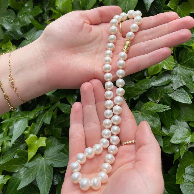 Two hands holding a white pearl necklace with a gold clasp 
