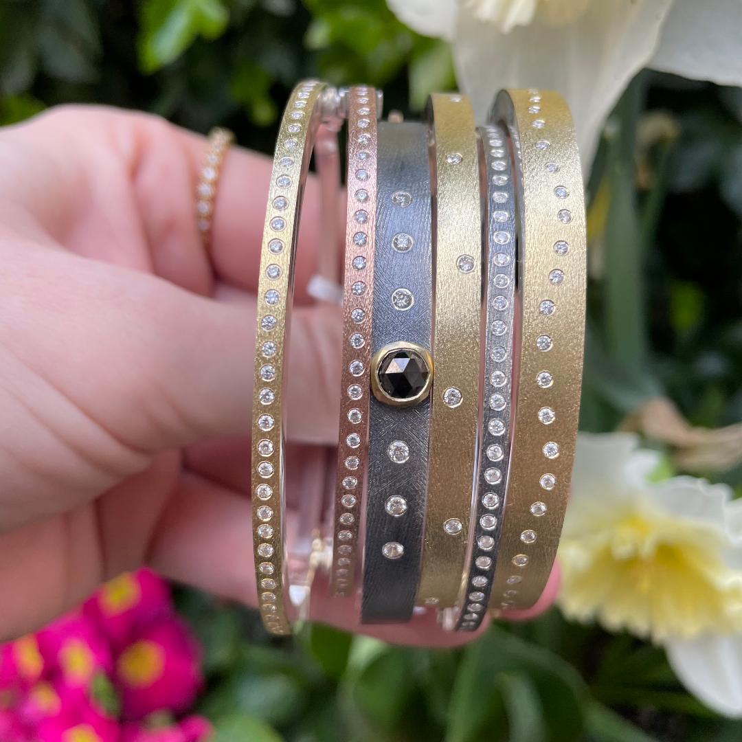 yellow, rose and white gold diamond bangles being held on a green leaf background