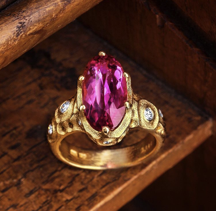 Pink tourmaline and yellow gold ring on wood background