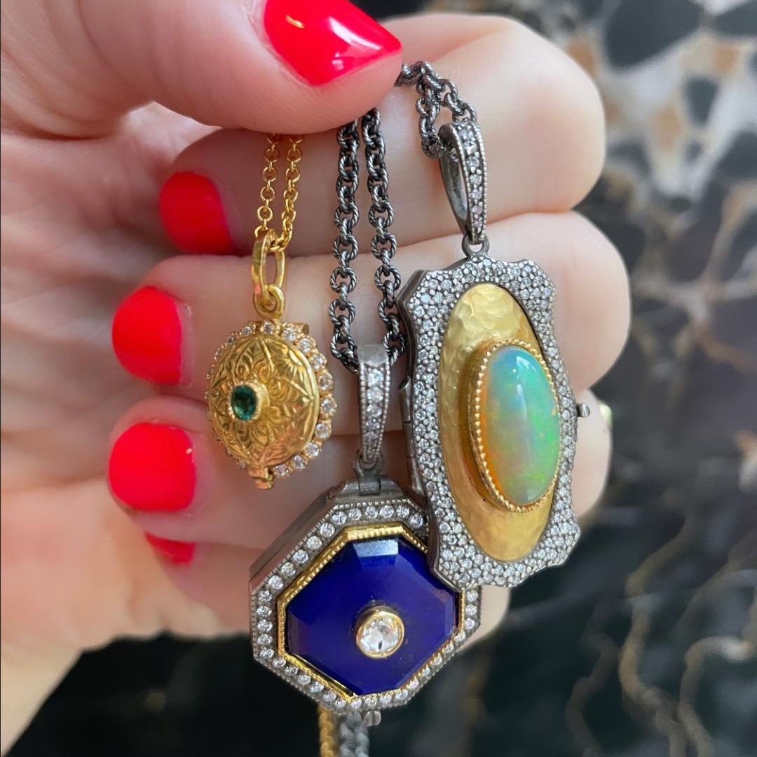 three necklaces being held in a hand with bright orange nail polish against a marble background