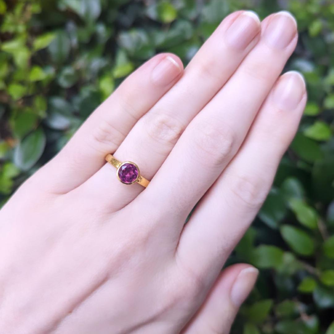 hand with pink gemstone ring in yellow gold over a green background