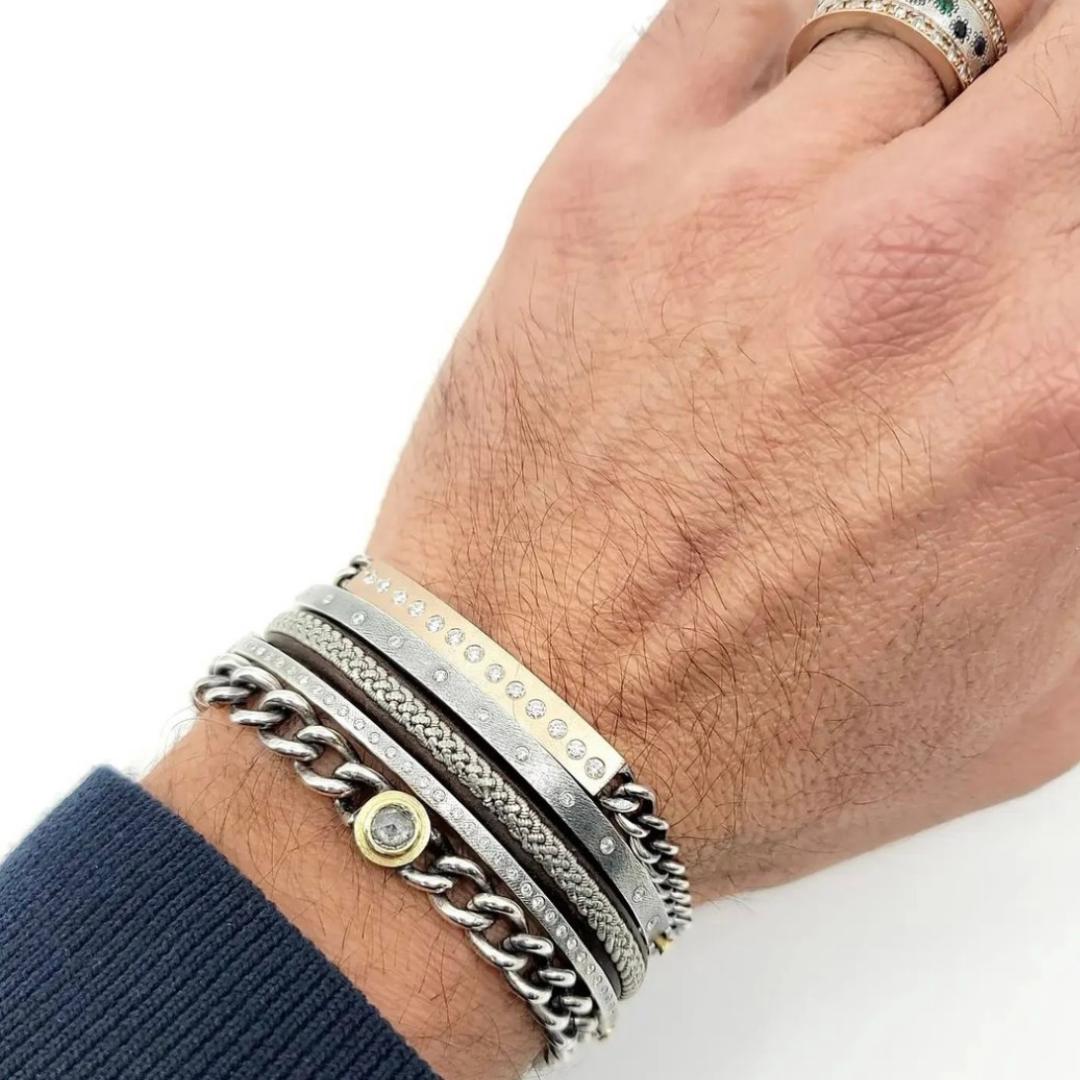 mens hand with multiple bracelets in silver and yellow gold