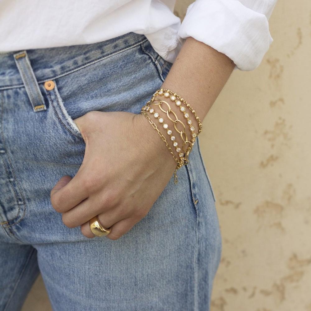 close up on woman wearing jeans and a white t-shirt with thumb in pocket. On wrist is 5 gold and diamond bracelets