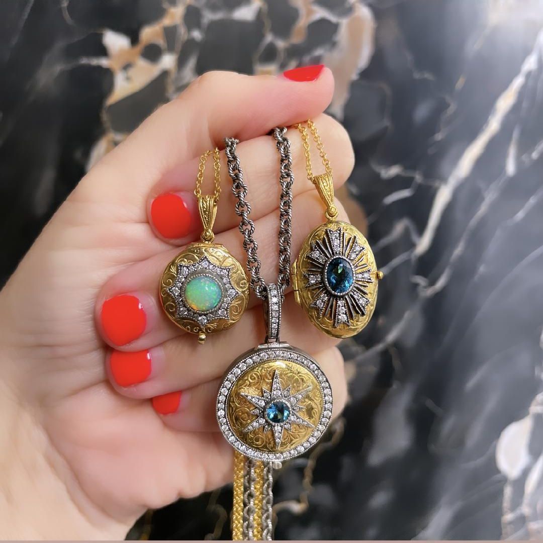 hand holding three pendants. Gold and tourmaline and gold and opal lockets.