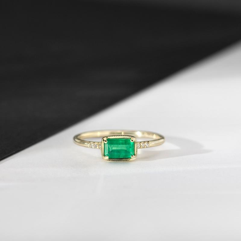 yellow gold emerald cut emerald ring with small diamonds on a white table with black background.