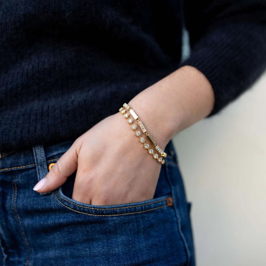 Hand in a pocket with two bracelets on. Body is wearing a black sweater and dark jeans.