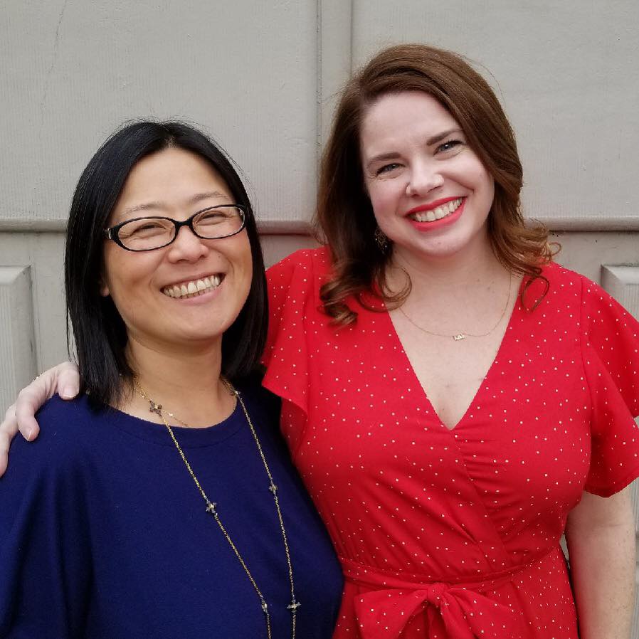 photo of two women smiling against the side of a building