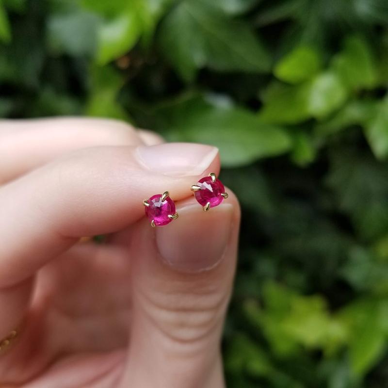 thumb and forefinger holding ruby earrings