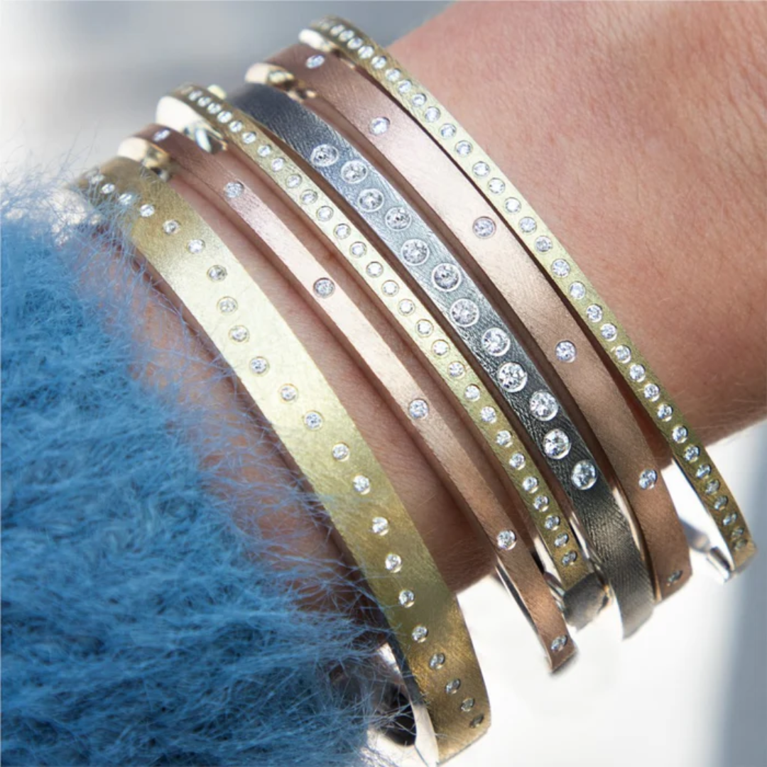 image of wrist with blue sweater and multiple bangle bracelets in white, rose and yellow gold with diamonds