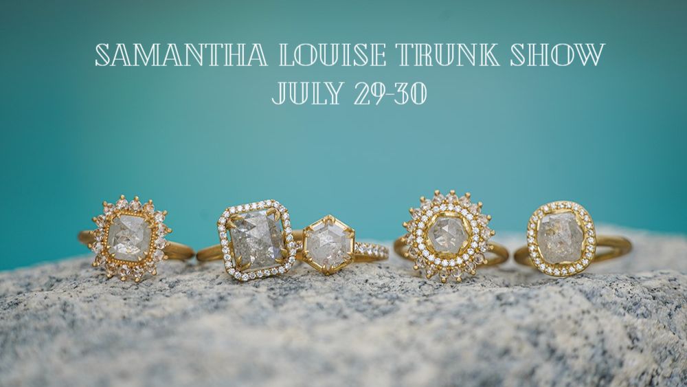 blue background with the words "Samantha Louise Trunk Show July 29-30" written above 5 yellow gold diamond rings sitting on a rock