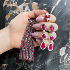 Hand holding ruby bracelet, ruby drop earrings, and ruby ring on dark marble background