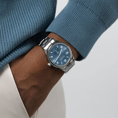 close  up on hip of person wearing blue sweater and white pants with a silver watch on the wrist with a blue dial