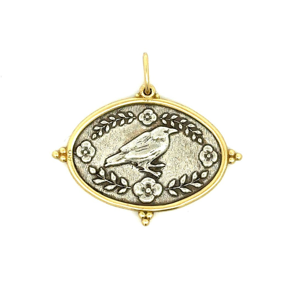 Erica Molinari sterling silver with 18k yellow gold rim raven charm front side showing the raven bird with flowers and leaf branches around. The charm is a large oval that is wider than it is long