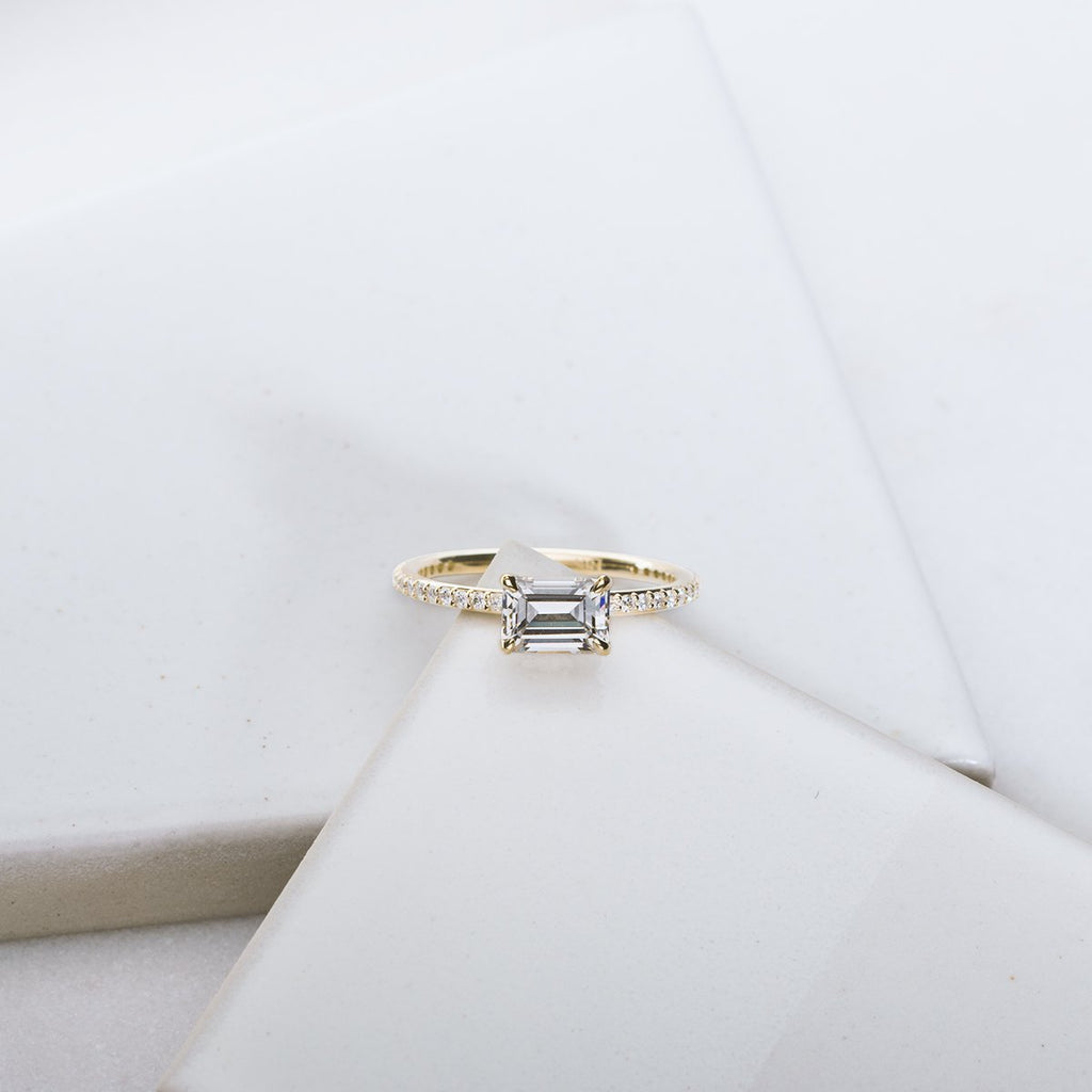 Engagement ring with rectangular diamond and pave diamonds along the yellow gold band