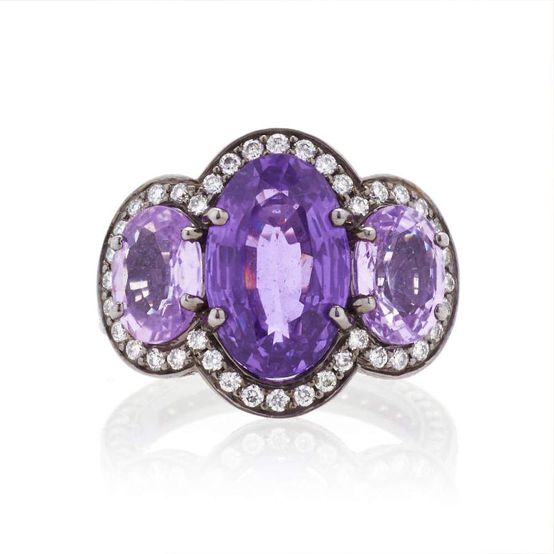 Bayco Jewels blackened platinum three stone ring comprised of 3 natural, unheated oval purple sapphires set within a colorless diamond micropave surround, with colorless diamond micropave on the gallery and shank