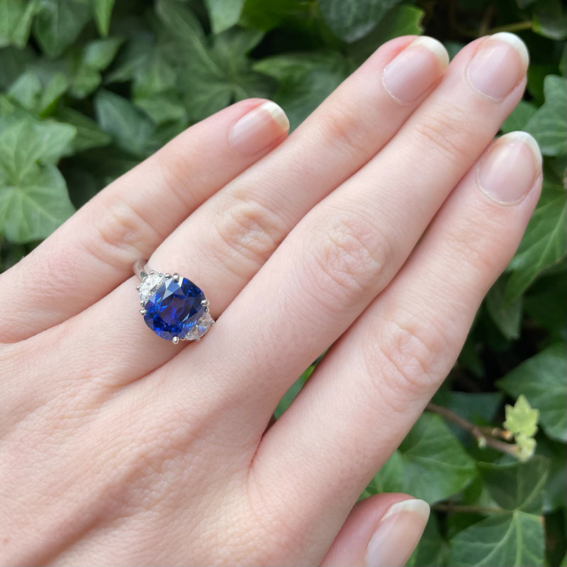 Bayco Jewels platinum ring centering a 5.11 carat cushion-shaped Madagascar sapphire flanked by two half moon diamonds on hand