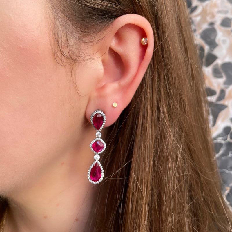 Bayco Jewels 18 karat blackened gold dangle earrings each set with a cushion-shaped Mozambique ruby set between two pear-shaped Mozambique rubies, all surrounded by micropavé set diamonds, pictured on model