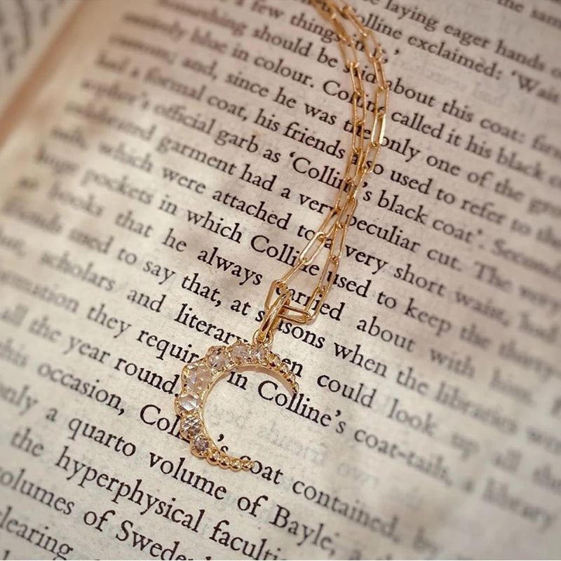 18K yellow gold "Crescent" rose cut diamond pendant with paper clip chain laying on top of newspaper
