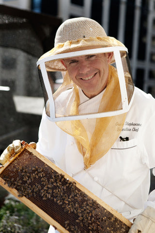 beekeeper, in full outfit, from Fairmont Olympic holding honey comb with bees all over.