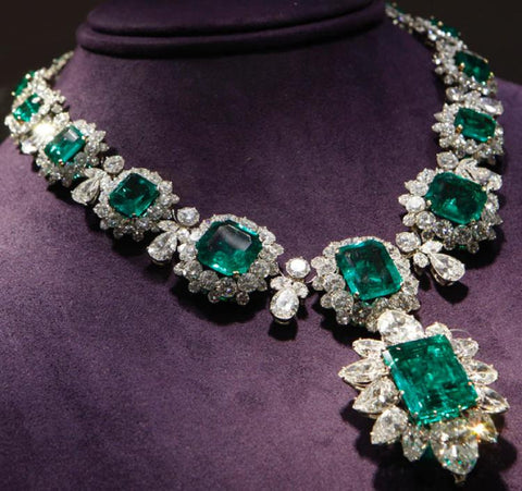 Large emerald and diamond estate necklace on purple neck form.