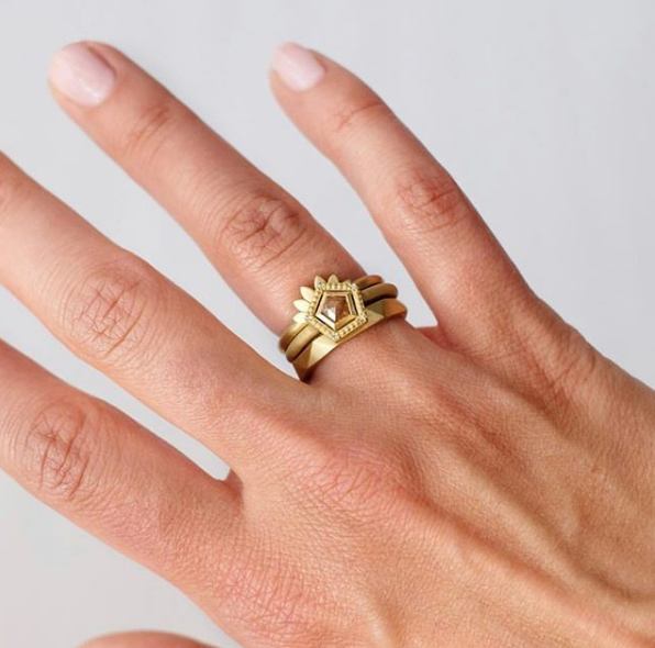 Woman's hand wearing 18K yellow gold thin Geo band in stack of two other rings